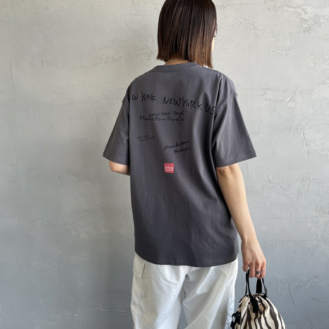 MANHATTAN PORTAGE [マンハッタンポーテージ] 別注 ランダムロゴ バックプリントTシャツ [25SSMP-IN66-JF] CHARCOAL &&モデル身長：159cm 着用サイズ：S&&